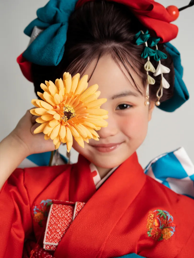 黄色い花を顔に添えて笑う赤い着物姿の女の子