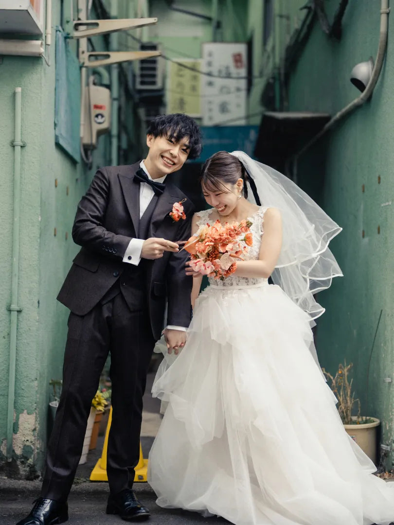 路地裏で花束を持つ新郎新婦が笑顔を交わすロケーションウェディングフォト。仙台フォトスタジオQnNe(キュンネ)