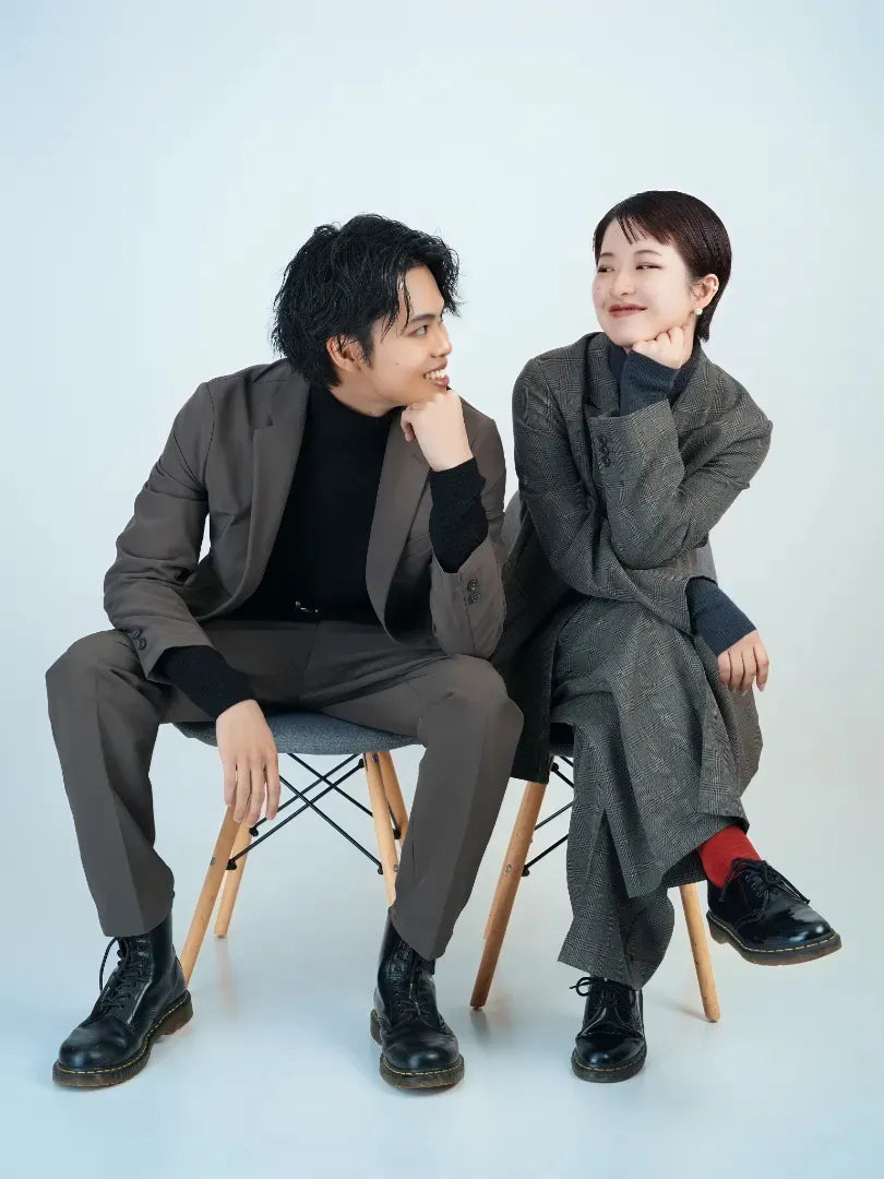 グレーのコーデをした男女が椅子に座り見つめ合って微笑むポートレート。仙台フォトスタジオQnNe(キュンネ)