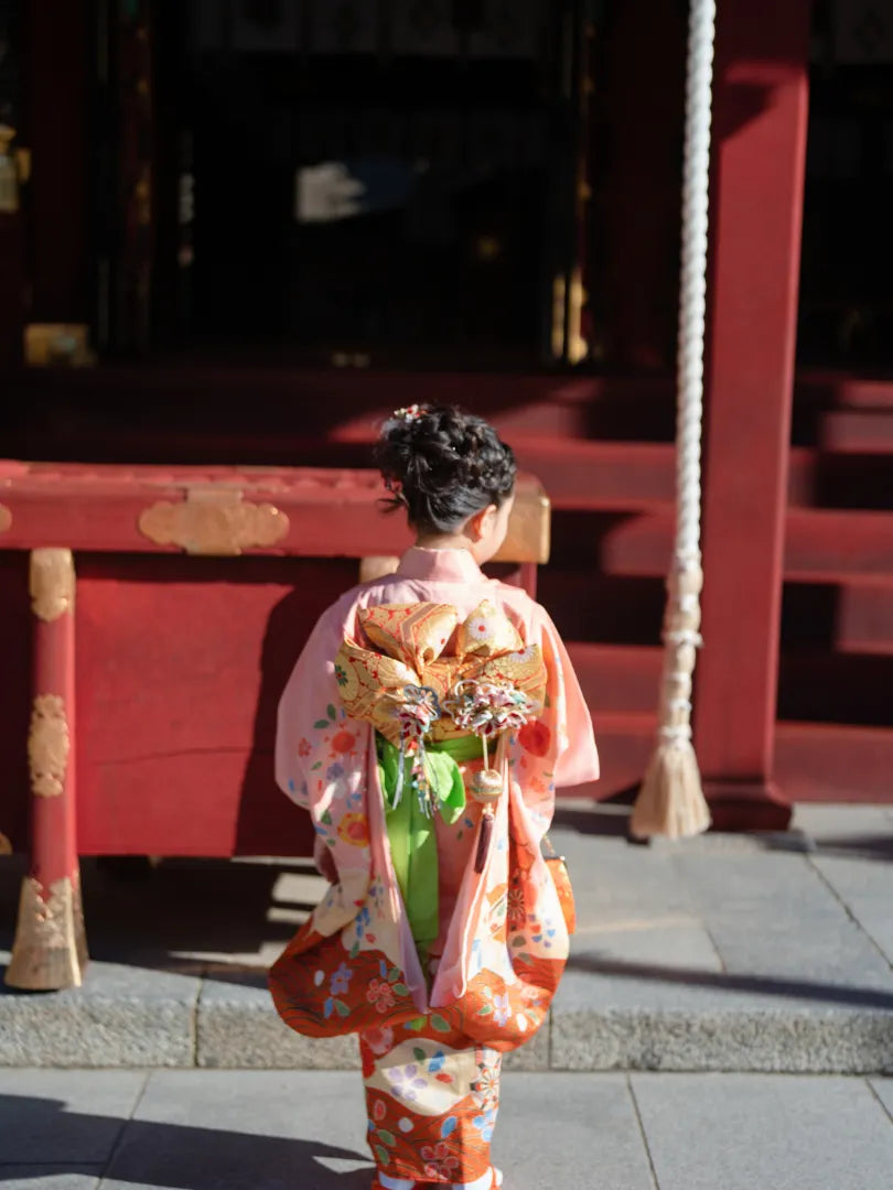 神社でピンクの着物を着た女の子が鈴の前で手を合わせる七五三フォト。仙台フォトスタジオQnNe(キュンネ)