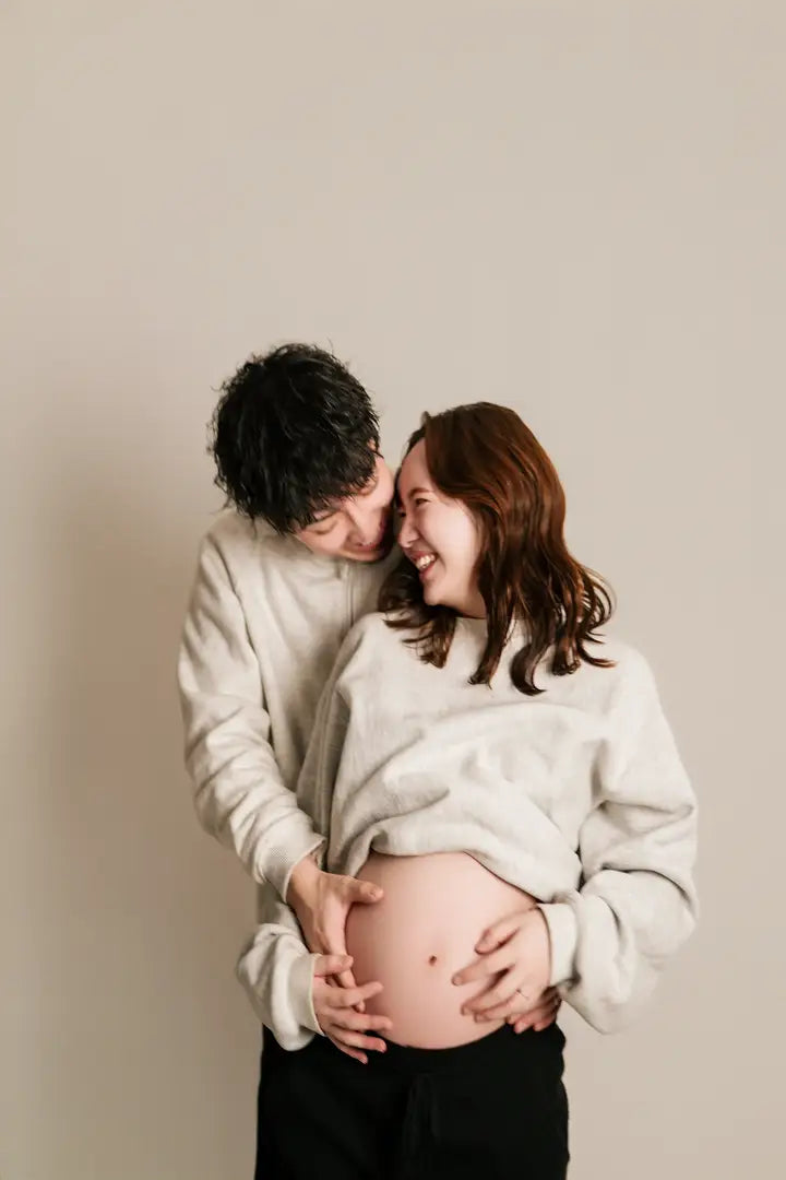 お腹に手を添えて笑い合うマタニティフォトの夫婦。仙台フォトスタジオQnNe(キュンネ)