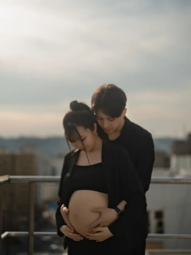 屋上で寄り添いお腹に手を添えるマタニティフォトの夫婦。仙台フォトスタジオQnNe(キュンネ)