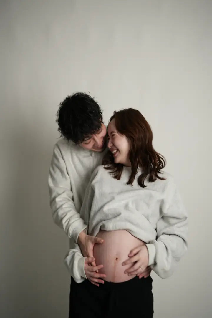 自然な笑顔で寄り添うマタニティフォトの夫婦。仙台フォトスタジオQnNe(キュンネ)