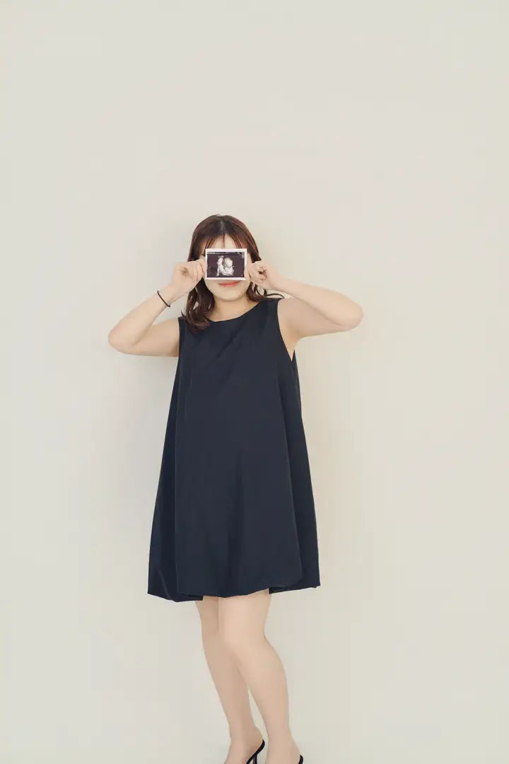 黒いワンピース姿の女性がエコー写真を持って微笑むマタニティフォト。仙台フォトスタジオQnNe(キュンネ)