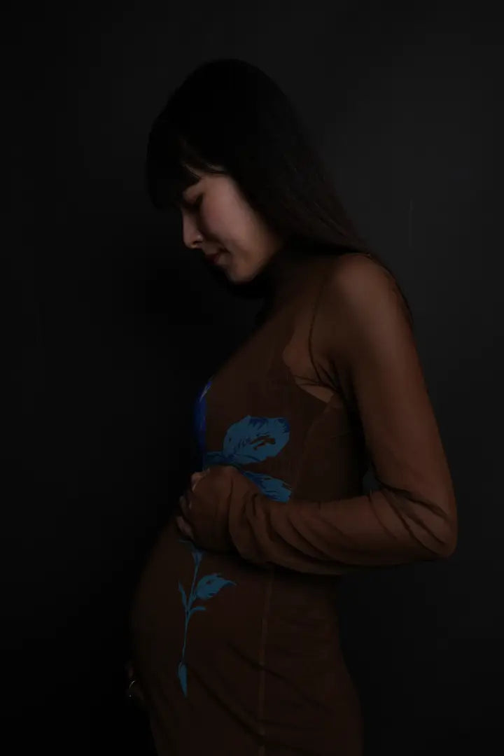 黒背景でブラウンのドレスを着た妊婦が穏やかにお腹を見つめるマタニティフォト。仙台フォトスタジオQnNe(キュンネ)