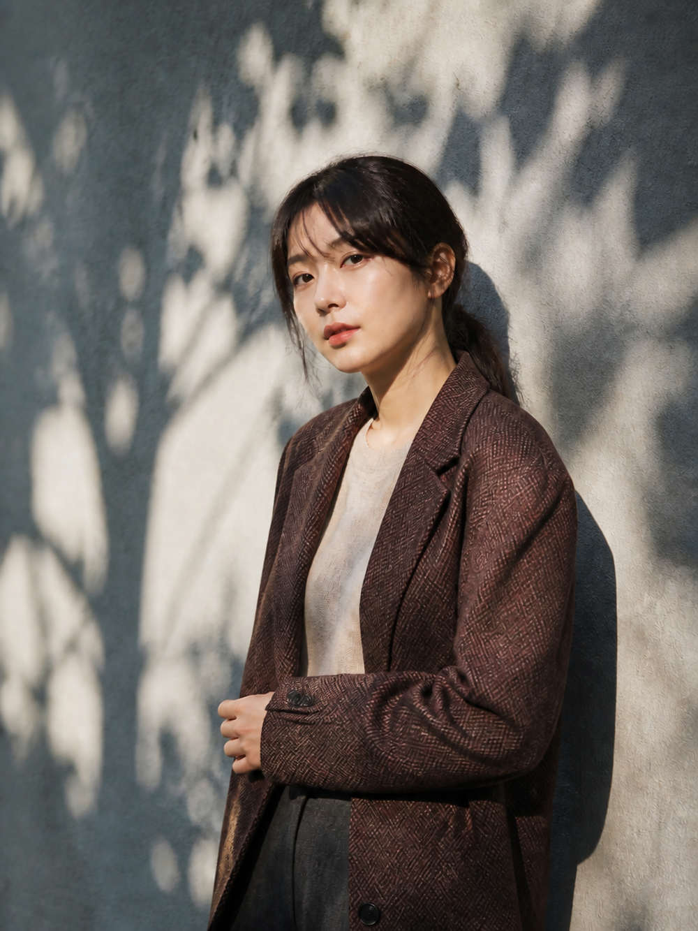 街なかの壁に落ちる木漏れ日の中で佇むバーガンディの服を着た日本人女性のポートレート