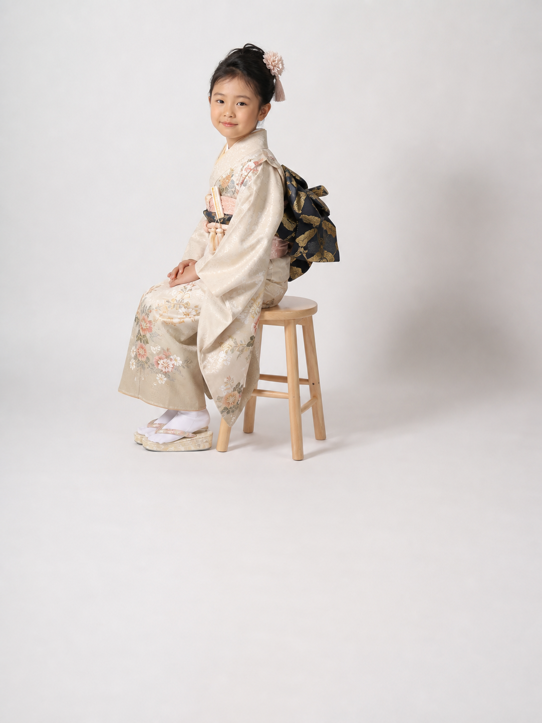 白いスタジオで木製スツールに座り振り返る七五三の着物姿の日本人の女の子｜仙台フォトスタジオQnNe