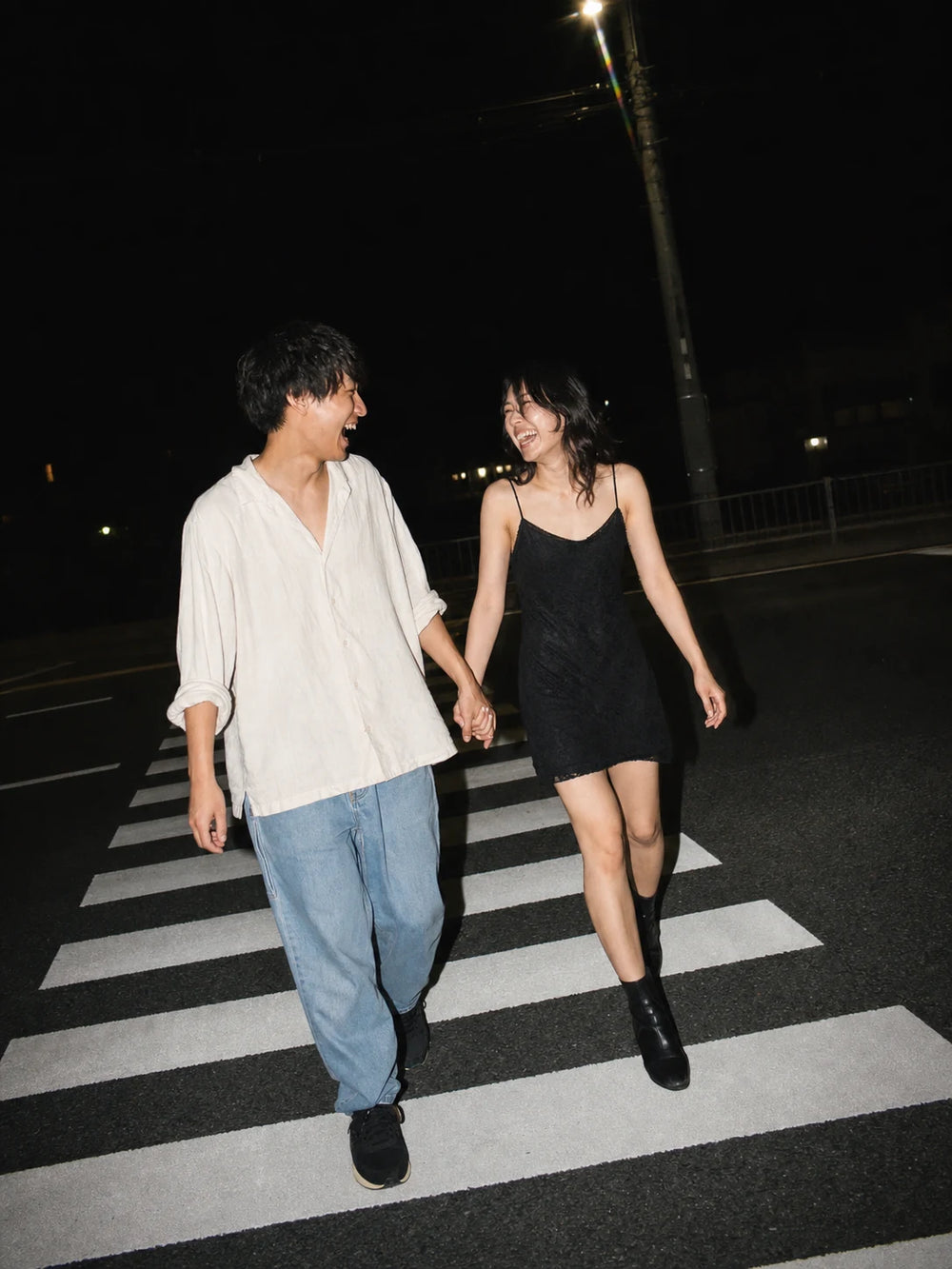 夜の横断歩道を手をつないで渡りながら笑い合うカップル｜仙台フォトスタジオQnNe（キュンネ）