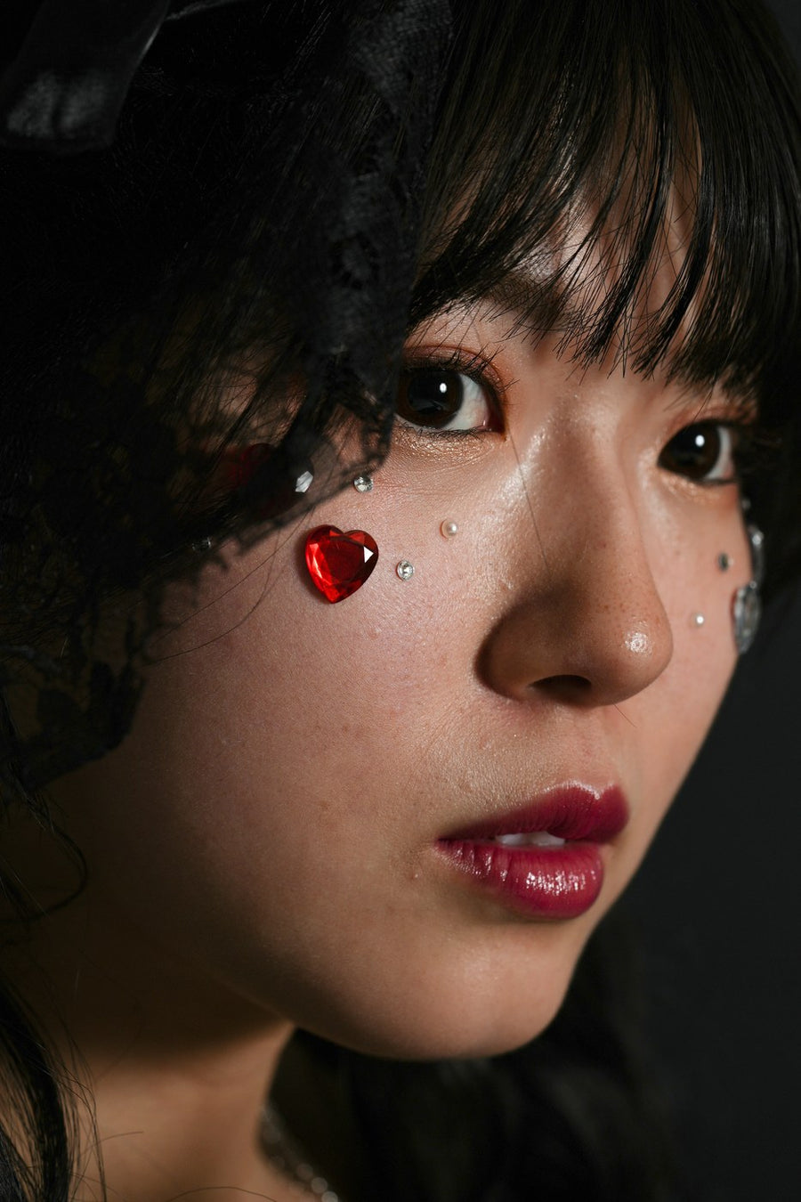 レタッチ前：黒いレースと赤いハートのフェイスジュエリーをつけた女性の顔のアップ（補正前）｜仙台フォトスタジオQnNe（キュンネ）