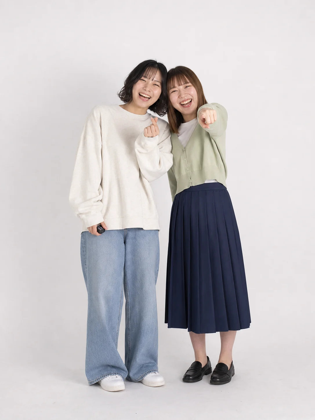 頭を寄せて指ハートと指さしをする友達同士のセルフフォト